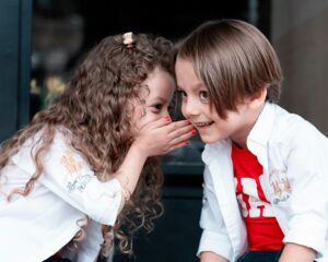 Children using language to communicate. One talking behind her hand to the other.